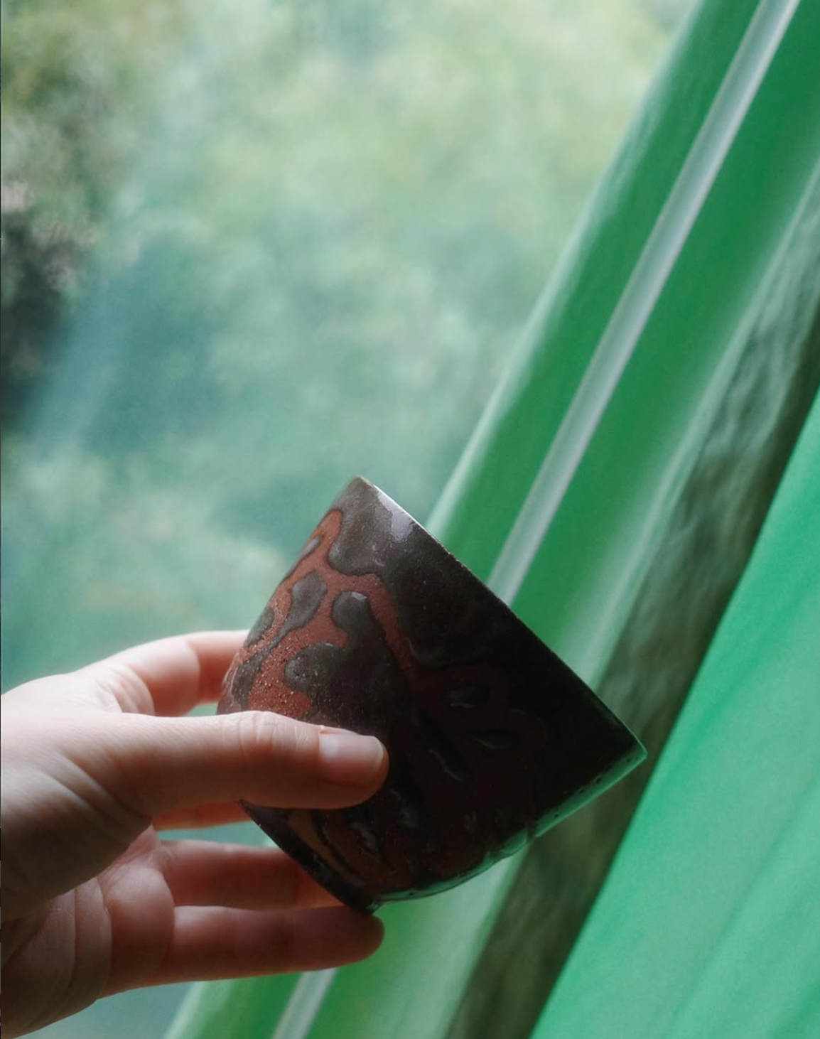 Handgedrehte Keramiknebel Lava-Tasse, ca. 190ml, mit dunkelbrauner, glänzender Glasur und einem erhabenen, leuchtend rotbraunen organischen Muster. Sie steht auf rauem, sonnenbeschienenem Stein und wirft einen definierten Schatten.